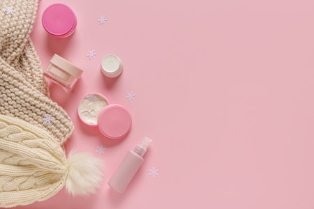 Jars of cream with snowflakes and warm winter clothes on pink backgroundの写真素材