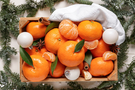Box of sweet mandarins with cinnamon, star anise, Christmas balls and fir branches on white wooden backgroundの写真素材