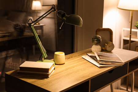 Modern workplace with glowing lamp, magazines and books in bedroom at nightの写真素材