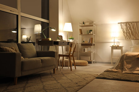 Interior of bedroom with workplace, sofa and glowing lamps at nightの写真素材