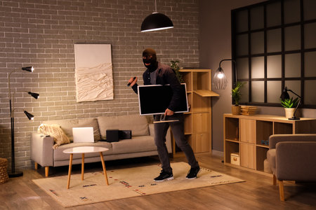 Male thief with flashlight stealing monitor in room at nightの写真素材