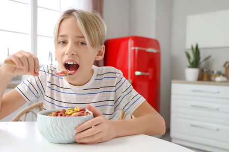 Cute little boy eating cereal rings at home