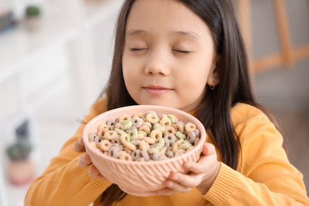 Cute little girl with bowl of cereal rings in kitchen, closeupの写真素材