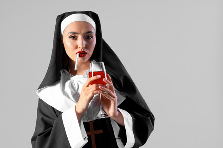 Naughty nun with glass of wine smoking cigarette on light backgroundの写真素材