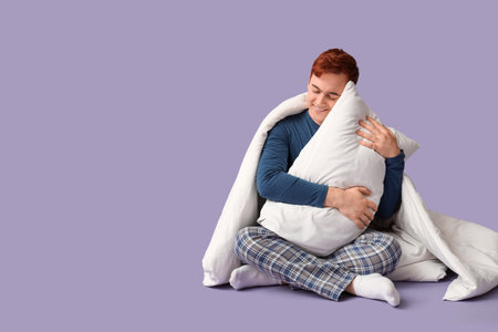 Handsome young happy man with blanket and pillow sitting on purple backgroundの写真素材