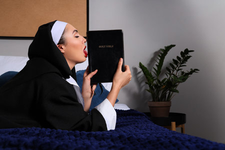 Sexy nun with Holy Bible lying in bedroomの写真素材