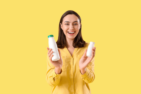 Happy young woman with bottles of tasty yoghurt on yellow backgroundの写真素材