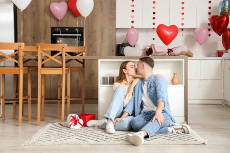 Beautiful young couple sitting on floor and celebrating Valentine's Day at homeの写真素材