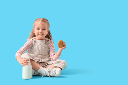 Cute little girl with bottle of milk and cookie sitting on blue backgroundの写真素材