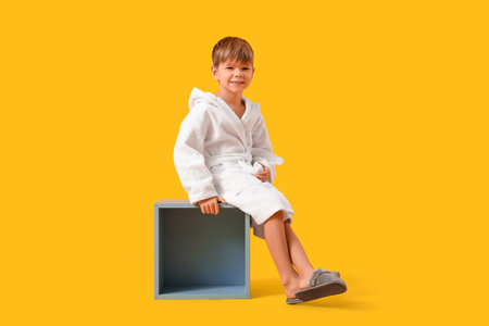 Cute little boy in bathrobe sitting on yellow backgroundの写真素材