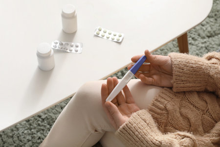 Woman with pregnancy test and pills on table at home, closeup