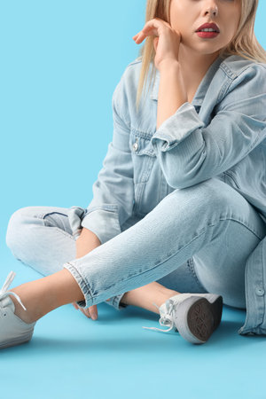 Stylish young woman in denim clothes sitting on blue backgroundの写真素材