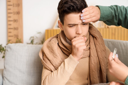 Mother with thermometer touching forehead of her sick little son at home
