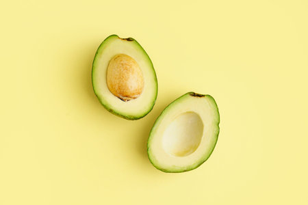 Halves of fresh ripe avocado on yellow backgroundの写真素材