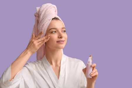 Beautiful woman in gown applying serum after shower on lilac background, closeupの写真素材