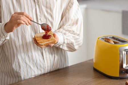 Young beautiful woman making tasty toasts with jam in kitchen, closeup