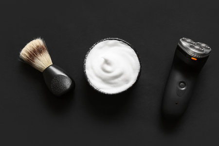 Bowl of shaving foam with brush and electric shaver on black backgroundの写真素材
