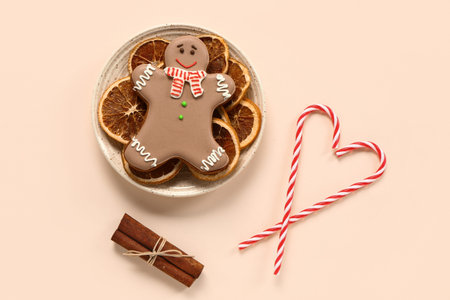 Plate of Christmas sweet gingerbread cookies with dried orange and candy canes on yellow background
