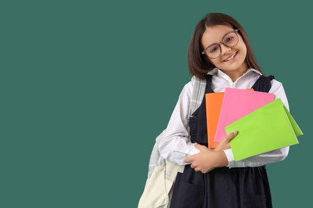 Little schoolgirl with copybooks and backpack on green backgroundの写真素材