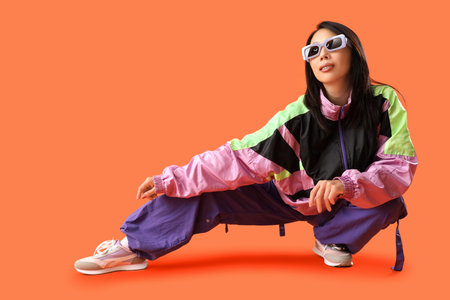 Beautiful stylish Asian woman in sunglasses posing on orange background