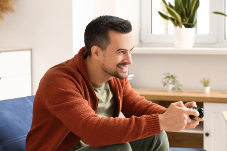 Handsome man playing video game on sofa in living roomの写真素材
