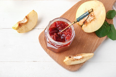 Board with jar of sweet jam and quince fruits on white wooden backgroundの写真素材