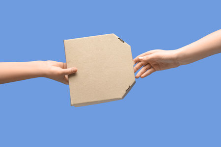 Female hands with takeaway cardboard pizza box on blue backgroundの写真素材