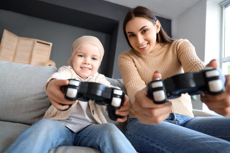 Little girl after chemotherapy with her mother playing video game at homeの写真素材