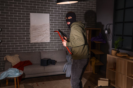 Scared male thief with crowbar and gun in room at nightの写真素材