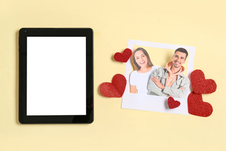 Photo of man with woman, tablet computer and paper hearts on yellow background. Concept of online datingの写真素材