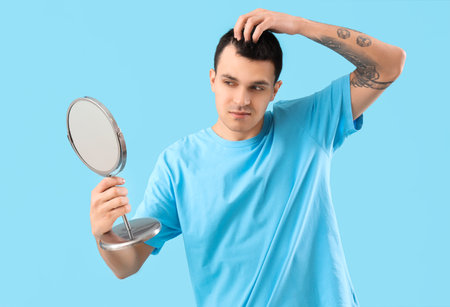 Young man with hair loss problem and mirror on blue backgroundの写真素材