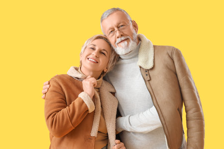 Mature couple in sheepskin coats hugging on yellow backgroundの写真素材