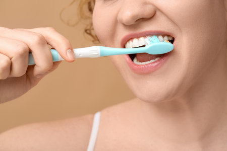 Beautiful young happy woman brushing teeth on brown background, closeupの写真素材
