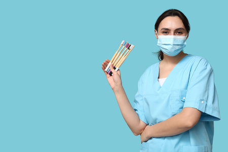 Young female dentist in mask with different toothbrushes on blue backgroundの写真素材