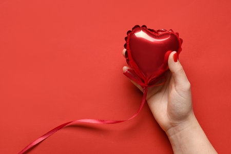 Female hand with red manicure and heart shaped balloon on color background. Valentine's Day celebrationの写真素材
