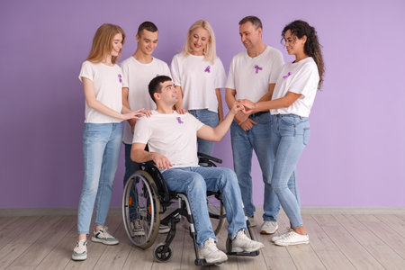 Young man in wheelchair and people with lavender awareness ribbons near color wall. World Cancer Dayの写真素材