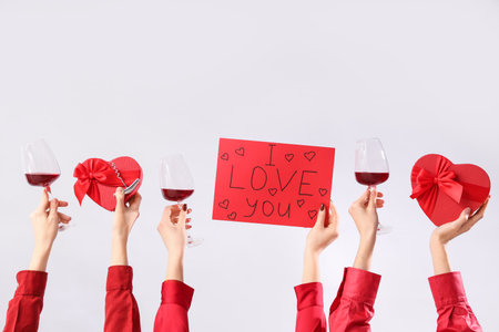 Women holding paper with text I LOVE YOU, red wine and gift boxes on light background. Valentine's Day celebrationの写真素材