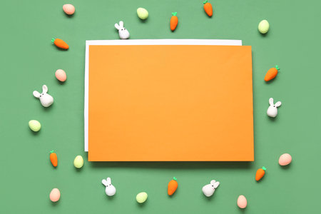 Easter bunnies, painted eggs, carrots and orange blank card on green background. Top viewの写真素材