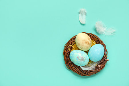 Nest with painted Easter eggs and feathers on turquoise background