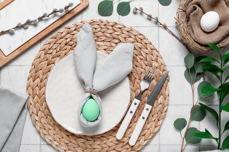 Beautiful table setting for Easter with eggs and green branches on white tile background
