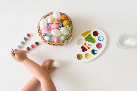 Little girl painting eggs for Easter on white background
