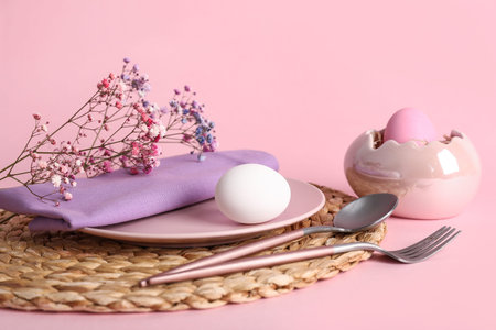 Beautiful festive table setting for Easter with eggs and flowers on pink background