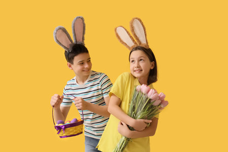 Little children in bunny ears with Easter eggs and tulips on yellow background