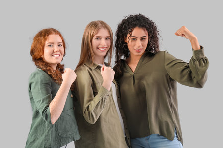 Beautiful young happy women showing muscles on gray background. Women history monthの写真素材