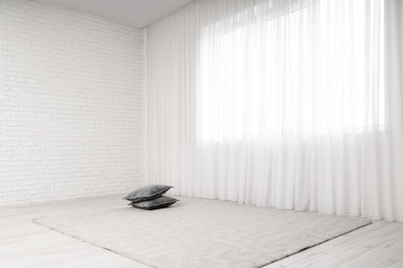 Cushions on floor with carpet near light curtain in living roomの写真素材