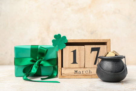 Leprechaun pot with golden coins, gift box and wooden calendar on beige grunge background. St....