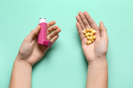 Child's hands with asthma inhaler and pills on turquoise backgroundの写真素材