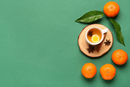 Wooden board with cup of tea, tasty tangerines and spices on green backgroundの写真素材