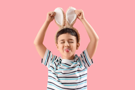 Funny little boy wearing bunny ears on pink background. Easter celebration