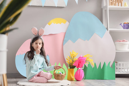Cute little girl with Easter basket showing silence gesture in festive room